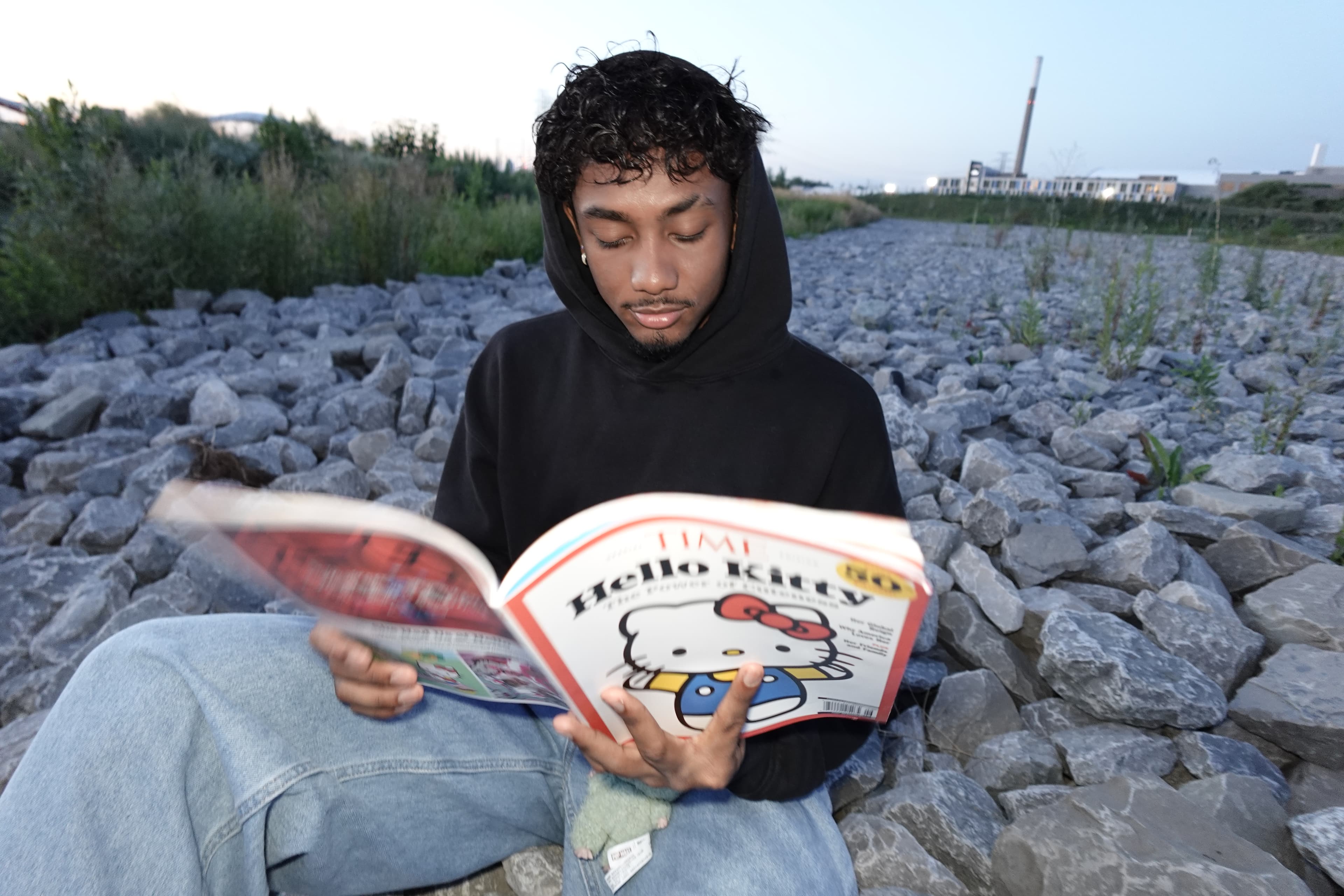Marco Hope sitting on a rocky riverbank at dusk, reading a magazine